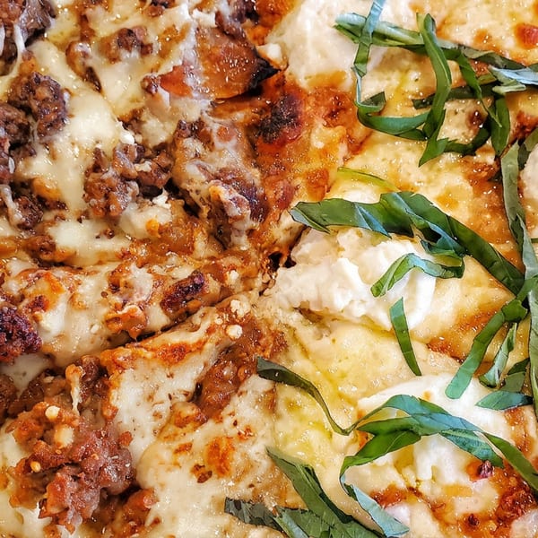 Close-up of a pizza with half covered in ground meat and the other half with basil and cheese.