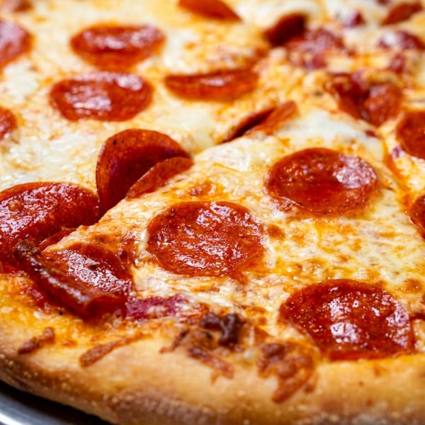 Close-up of a freshly baked pepperoni pizza with melted cheese on a metal tray.