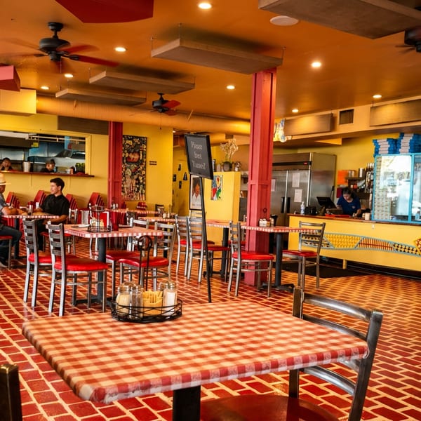 Vibrant restaurant interior with red and yellow decor, checkered tablecloths, and patrons dining.