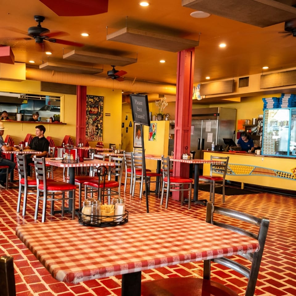 Vibrant restaurant interior with red and yellow decor, checkered tablecloths, and patrons dining.