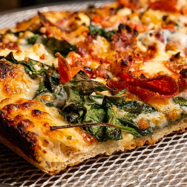 Close-up of a rectangular pizza slice with pepperoni, spinach, and cheese on a metal tray.