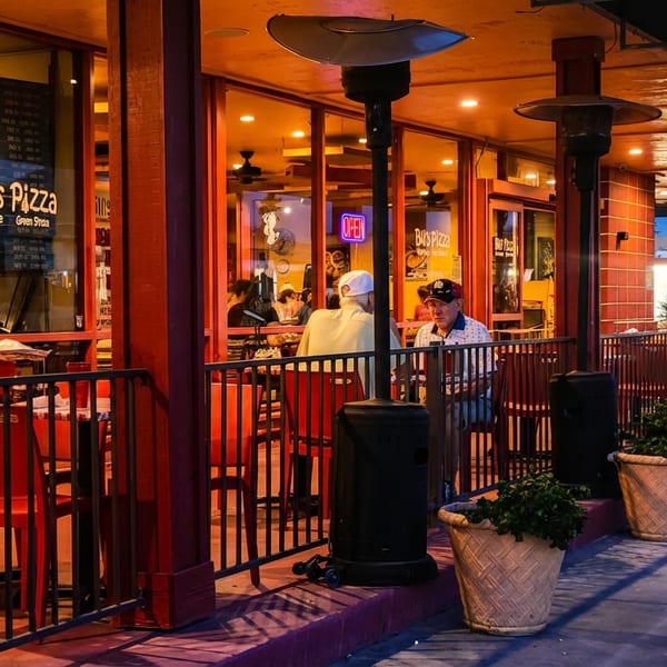 Bill's Pizza restaurant exterior at dusk with outdoor seating, patrons, and warm lighting.